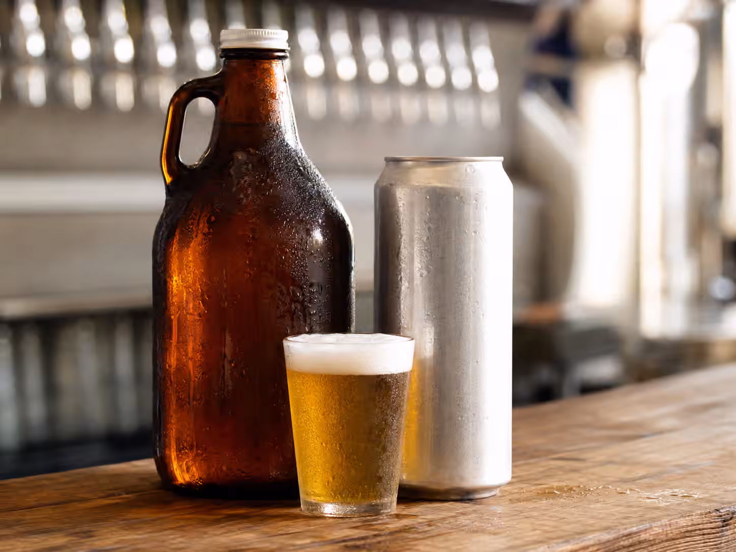 An amber growler and plain crowler can on a brewery counter with a fresh glass of beer.