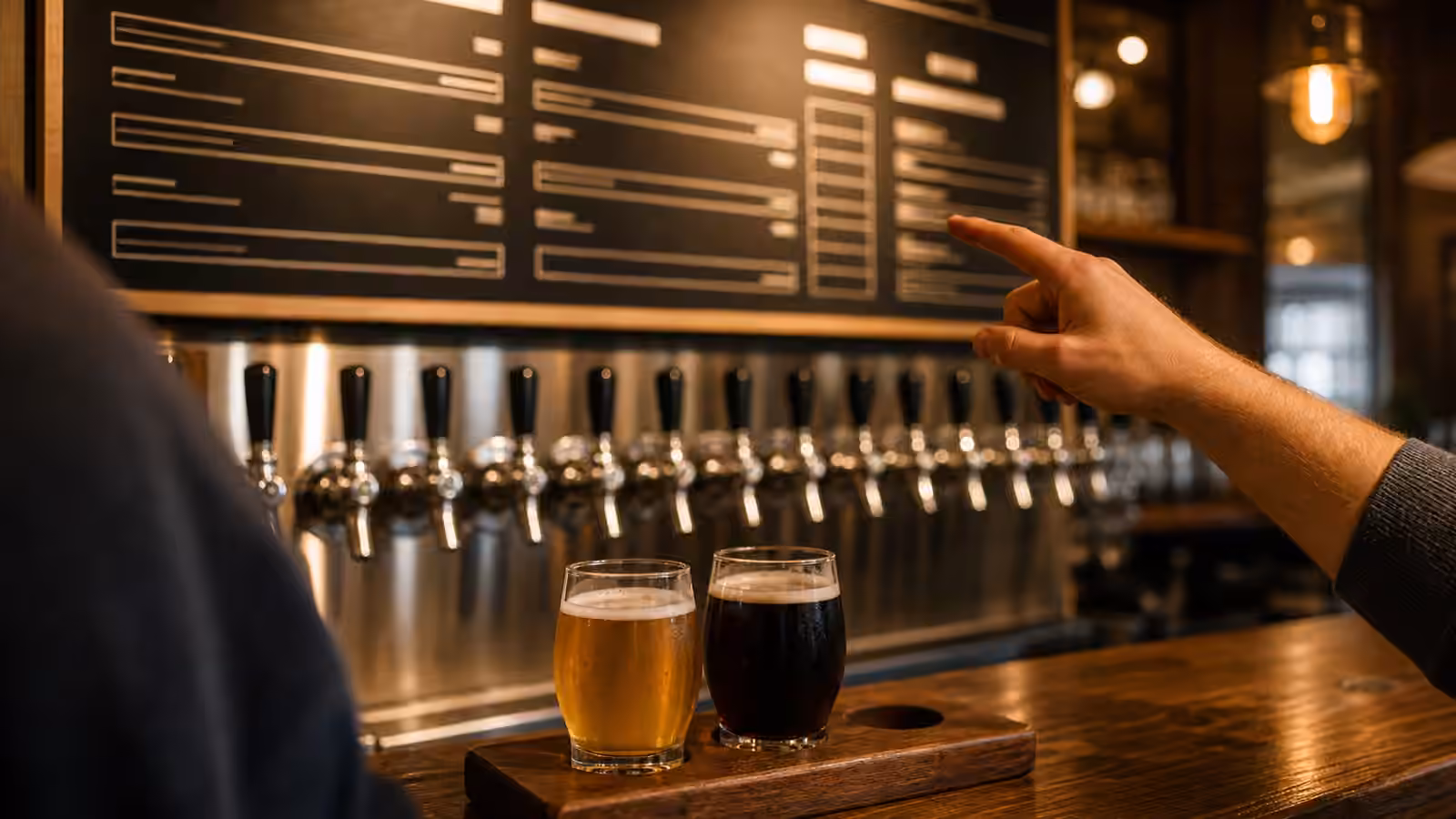 Unbranded tap handles and a blurred taproom menu behind two small beer pours.