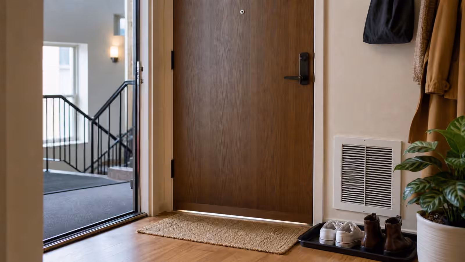 An apartment entry door with a door sweep, washable mat, shoe tray, nearby vent, and soft hallway light.