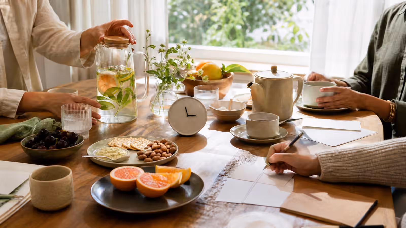 a bright daytime table with tea, citrus water, simple snacks, blank note cards, and a small clock