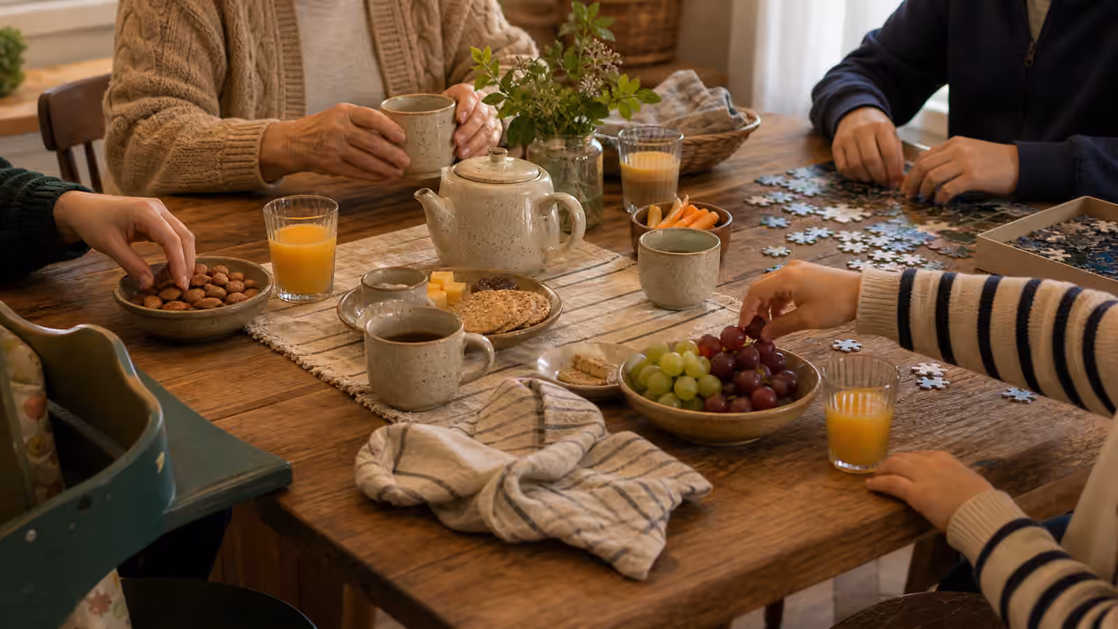 mixed-age hands sharing tea, juice, snacks, puzzle pieces, and simple table tasks in daylight