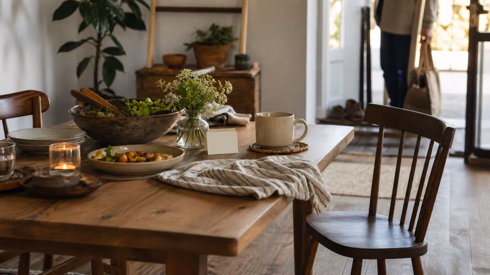 a warm table with food, a waiting mug, a blank place card, an open spare chair, and a softly lit entryway