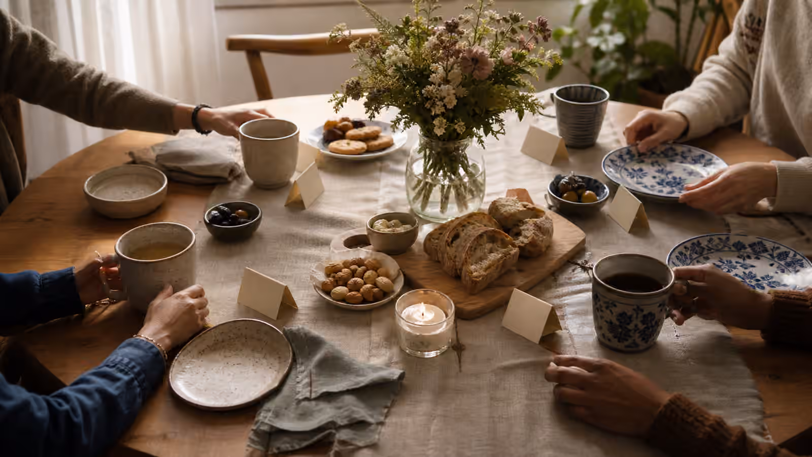 a small table where two sets of cups and snack plates meet around tea, bread, blank place cards, and angled chairs