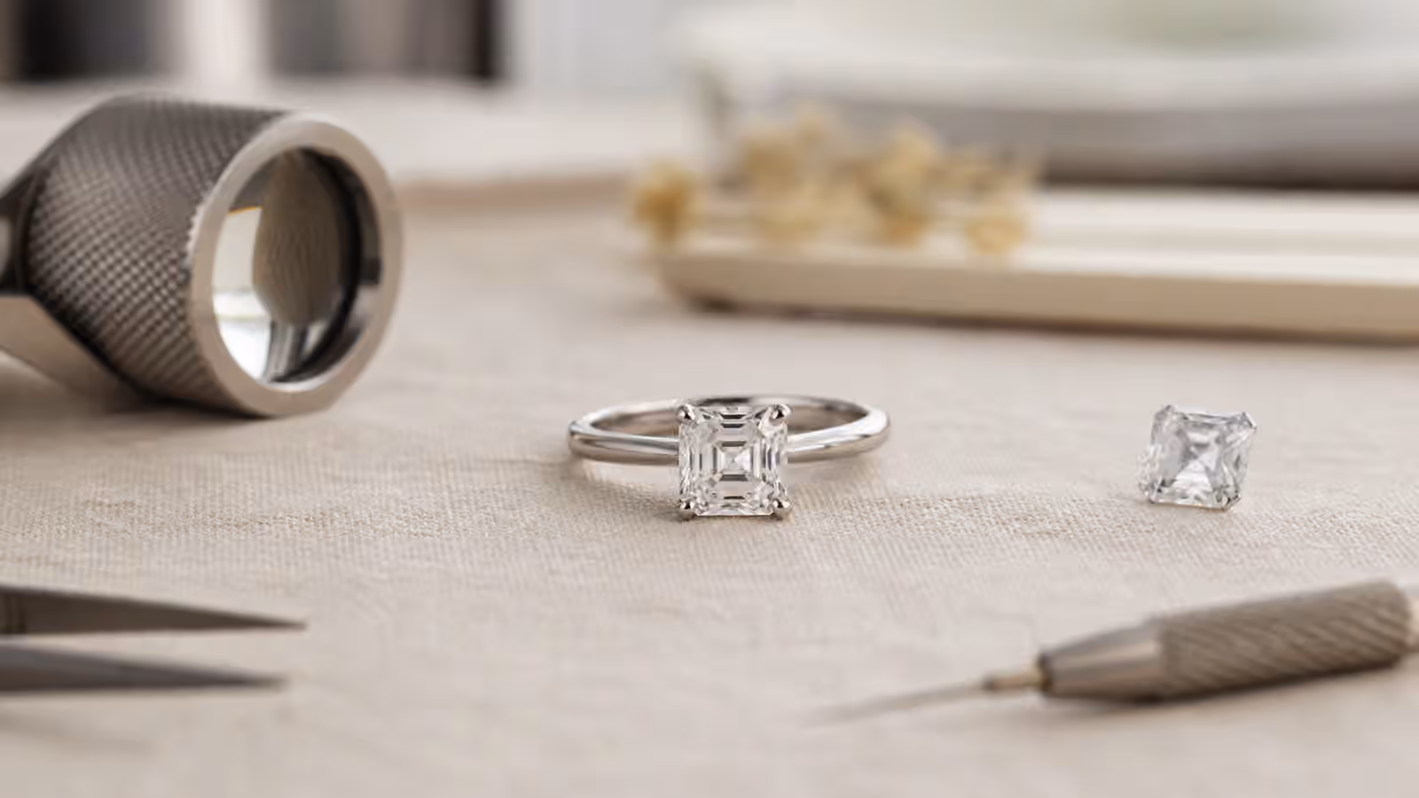 Asscher-cut diamond engagement ring with a loose square step-cut diamond and jeweler's loupe.