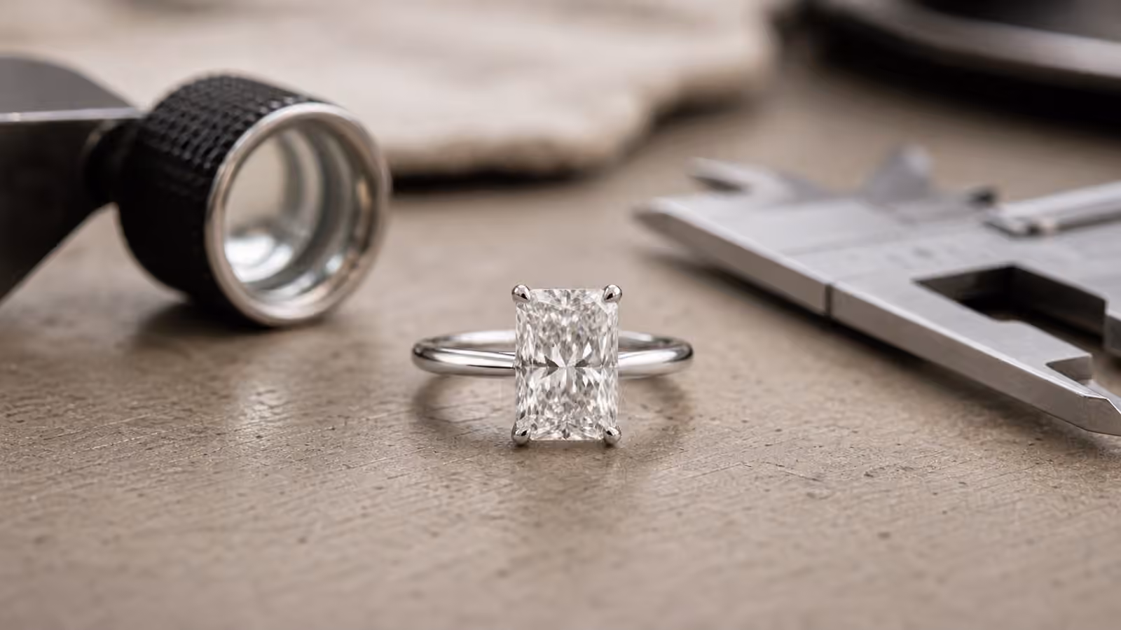 Radiant-cut diamond engagement ring on a jeweler's bench with calipers nearby.