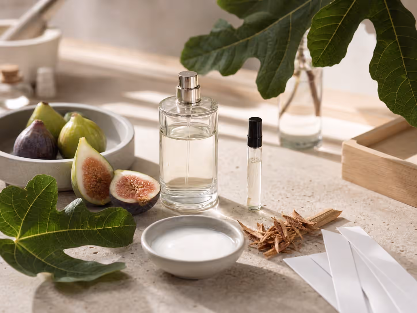 An unbranded perfume bottle with fig leaves, sliced figs, milky sap in a dish, cedar shavings, blotters, and a sample vial.