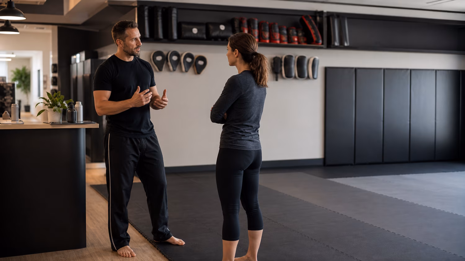A calm Krav Maga studio where an instructor talks with a prospective student near the training floor.