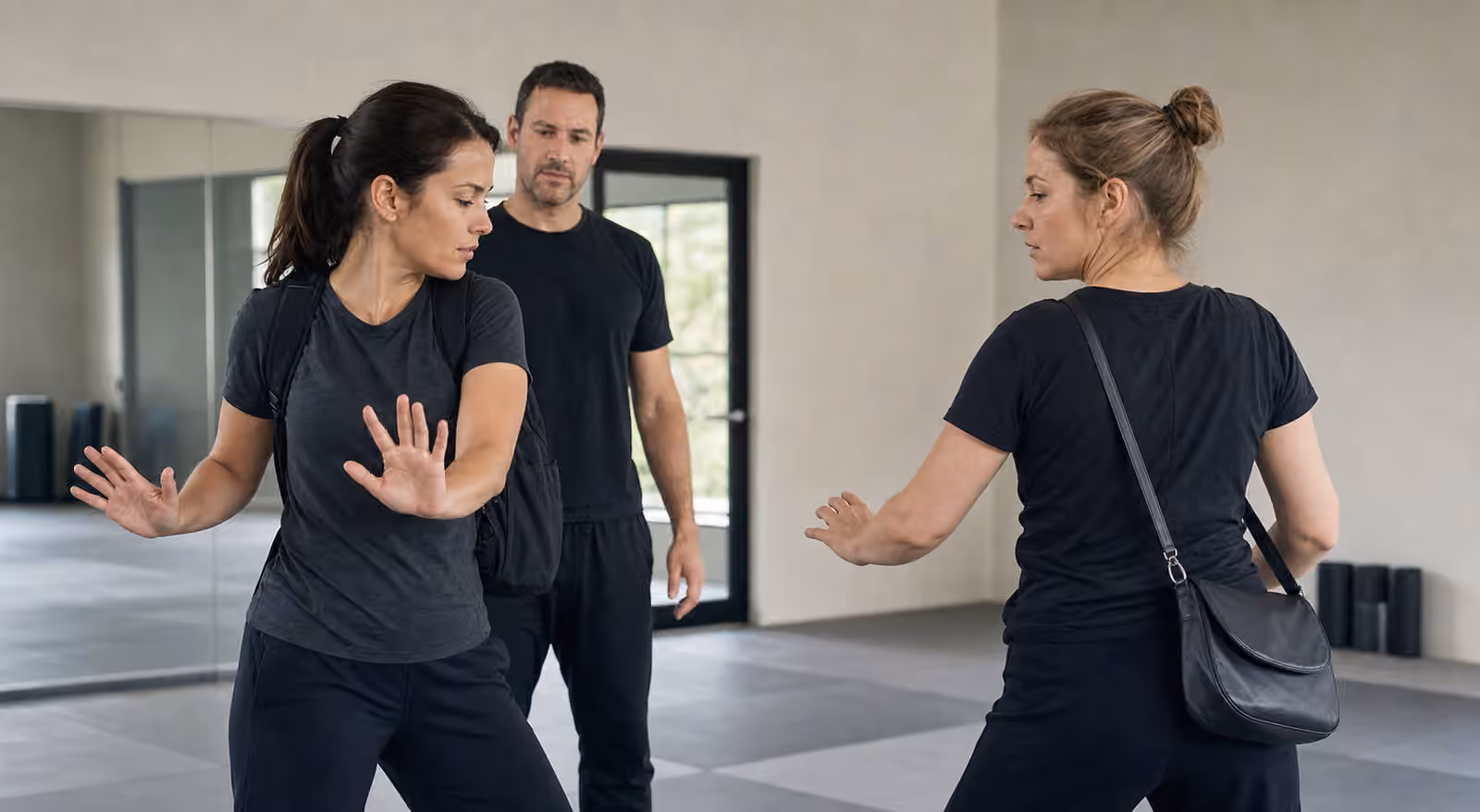 Adult Krav Maga students practice calm movement and open-hand posture while a shoulder bag changes spacing.