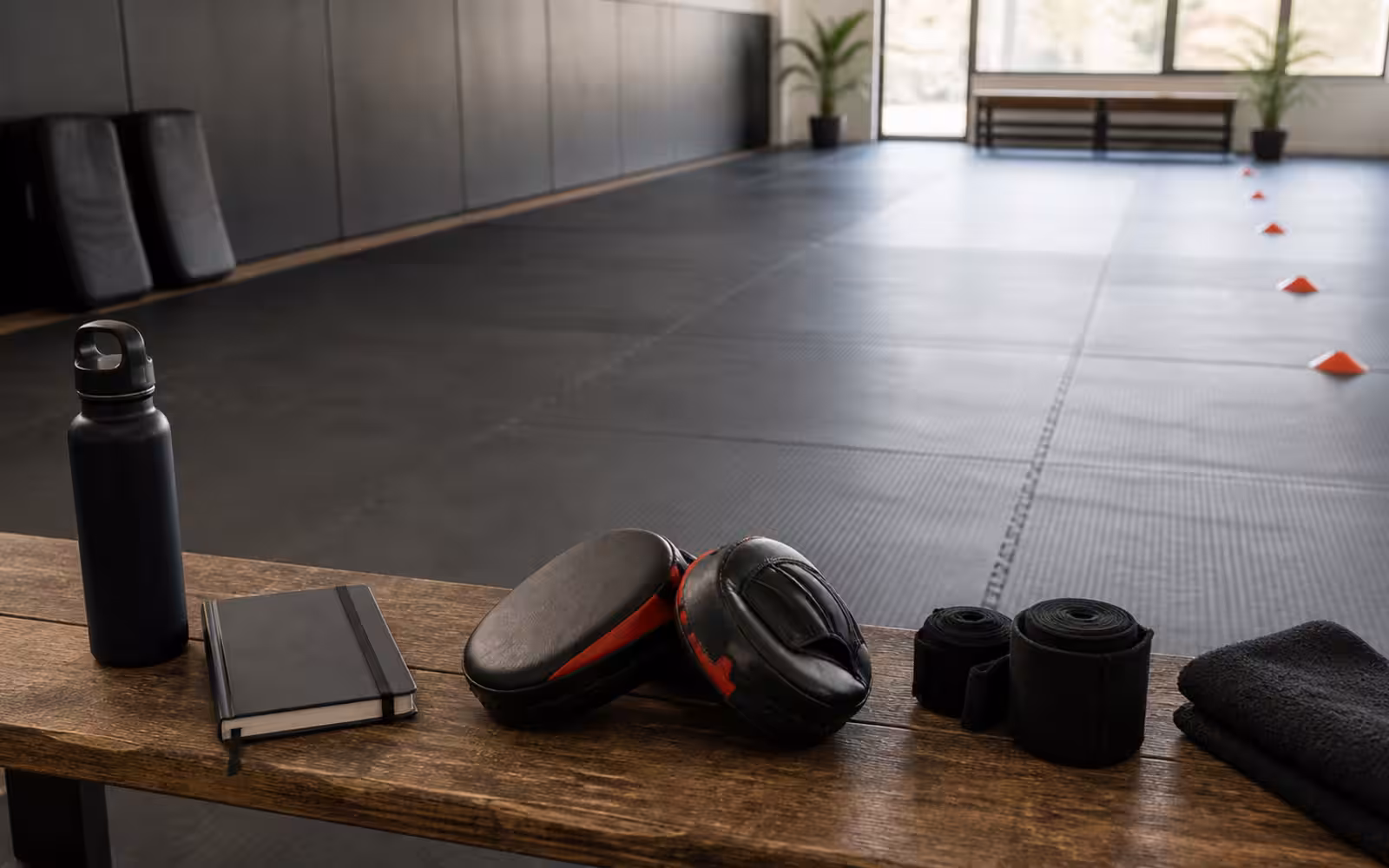 A Krav Maga guidebook hero scene with training pads, notebooks, wraps, cones, and a quiet studio floor ready for adult beginners