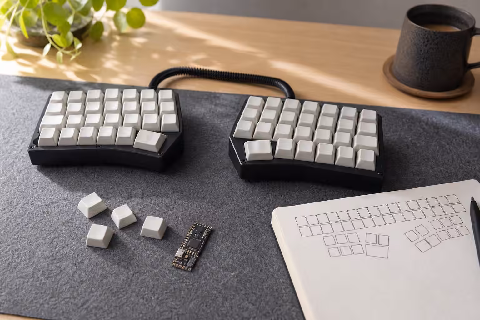 Compact split keyboard with blank keycaps, thumb keys, and an abstract keymap notebook.