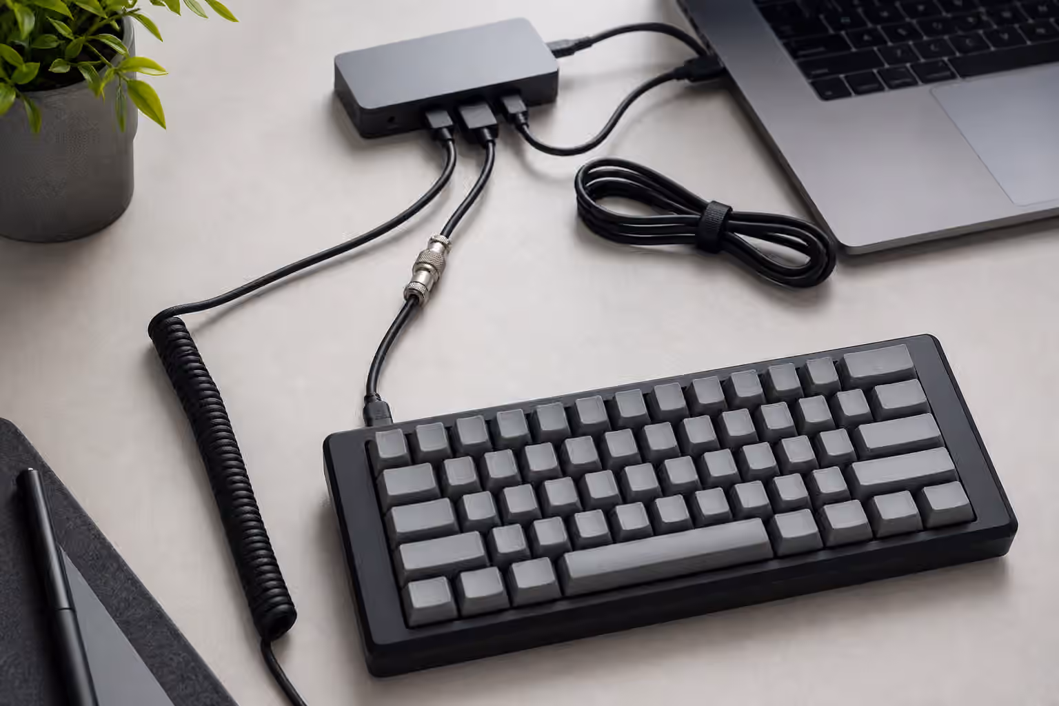 Mechanical keyboard connected to a laptop through a coiled USB-C cable with spare cable, hub, and cable tie.