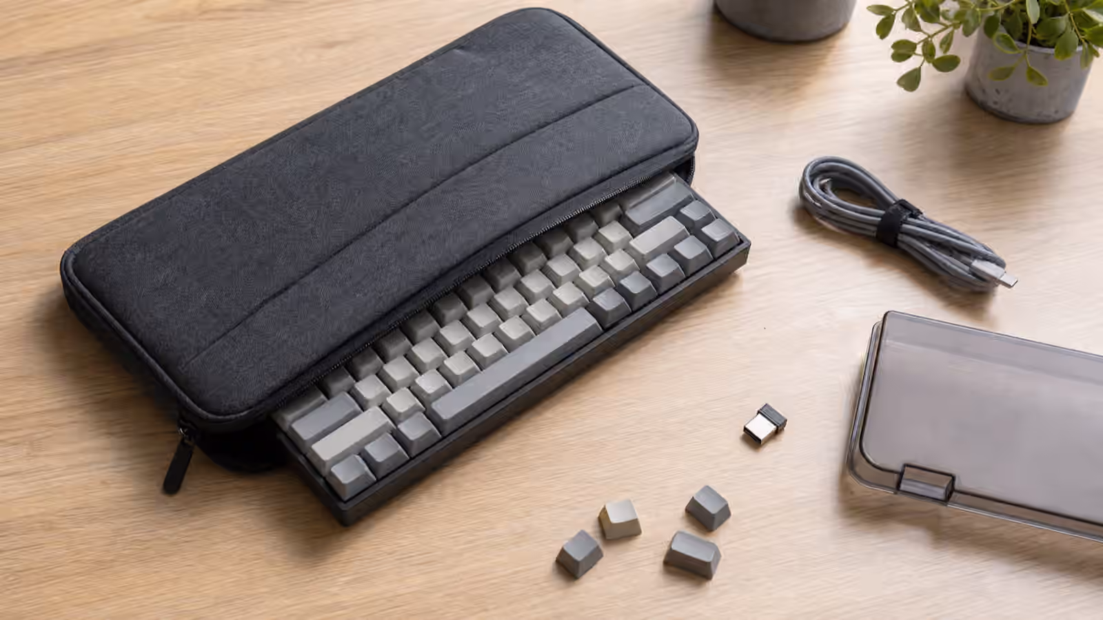 Compact mechanical keyboard partly inside a padded travel case with cable, dongle, dust cover, and loose keycaps.