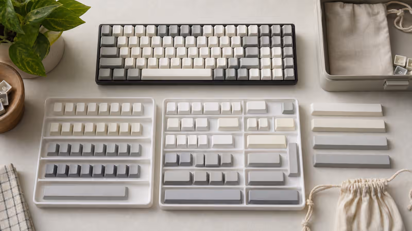 Blank keycaps sorted in trays beside a compact keyboard, storage box, cloth bags, and spacebars on a tidy desk.