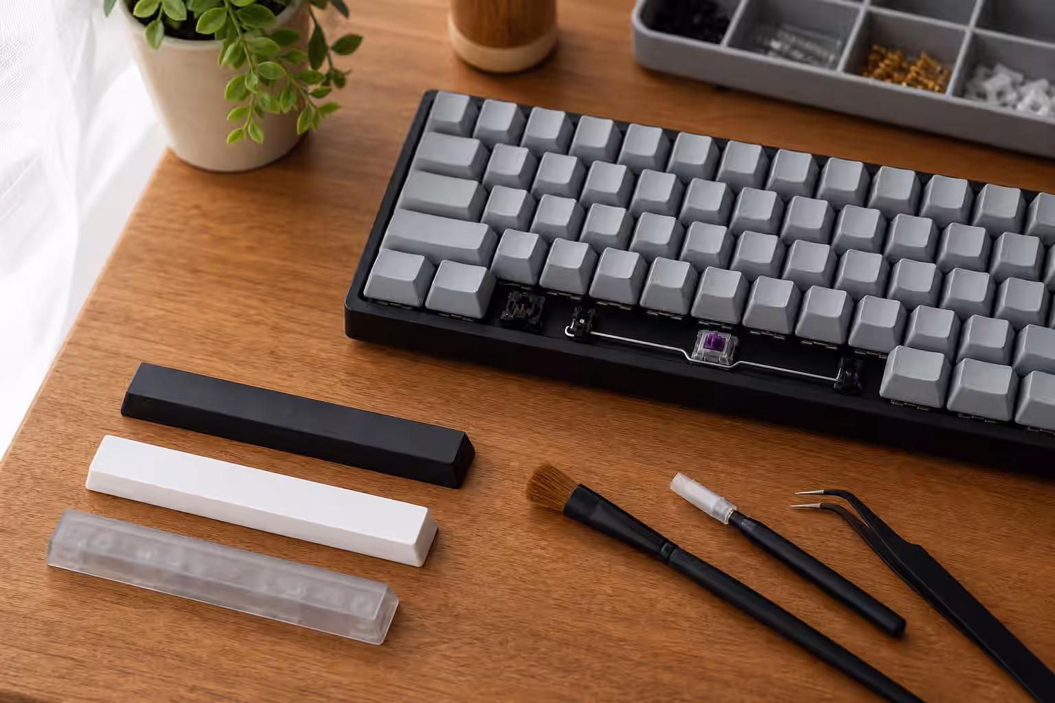 Mechanical keyboard with spacebar removed, visible stabilizer parts, tools, and spare blank spacebars.