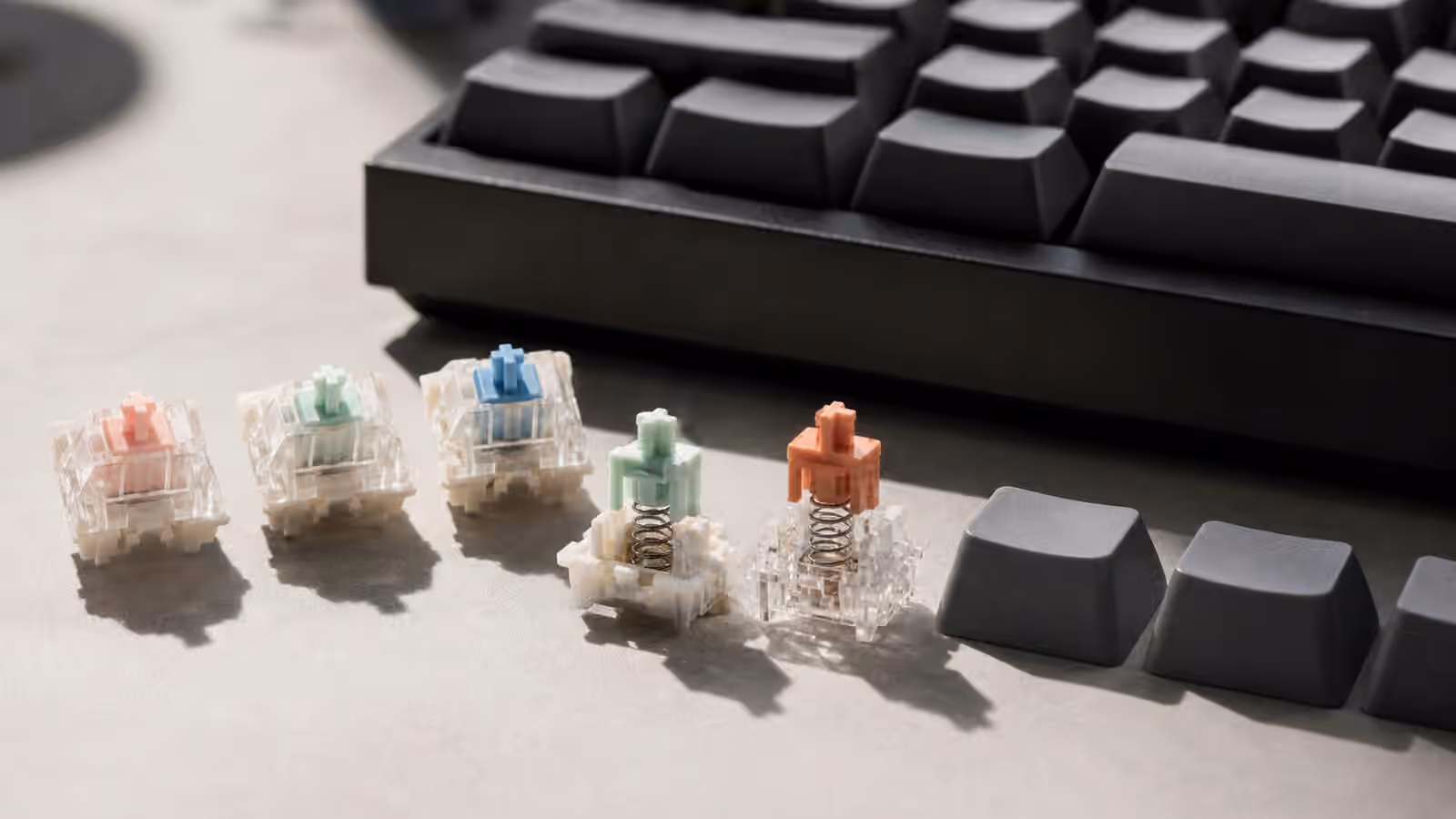 Loose mechanical keyboard switches, opened switch housings, springs, stems, and blank keycaps beside a compact keyboard.