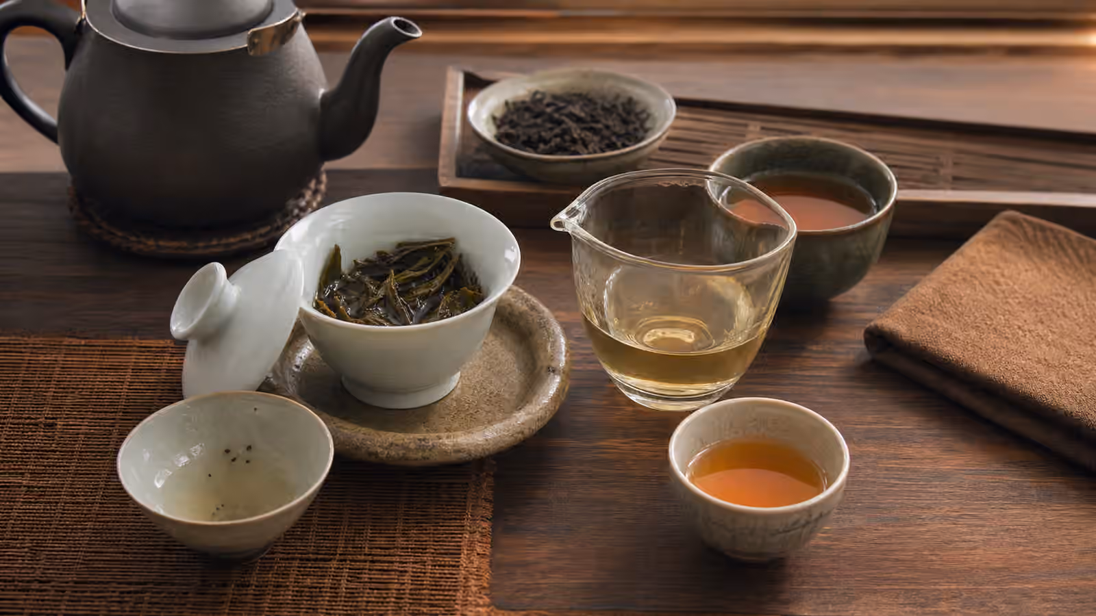Gaiwan with wet leaves, a small rinse cup, a fairness pitcher, and amber tea cups.